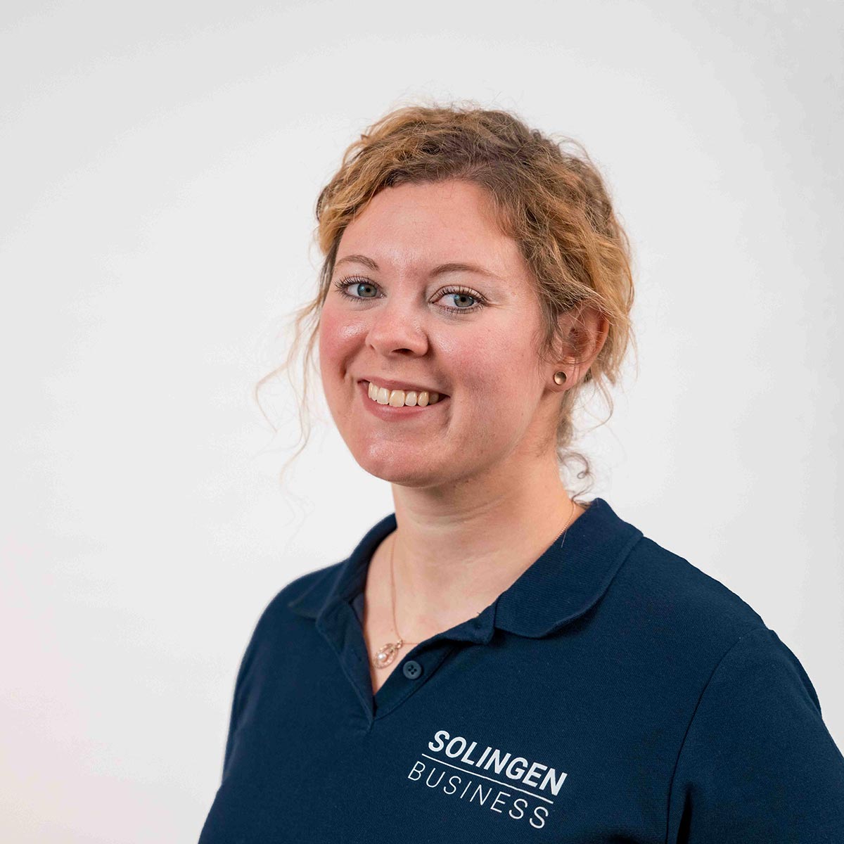 Porträt von Leonie Schubert, Teammitglied von Solingen.Business, in blauem Poloshirt vor hellem Hintergrund