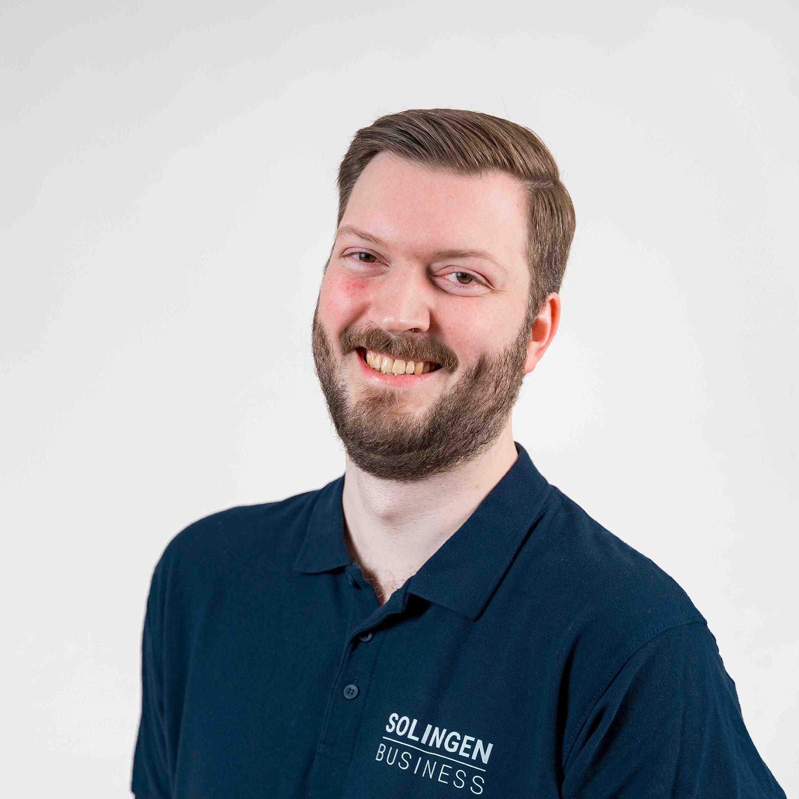 Porträt von Marius Borkenhagen, Teammitglied von Solingen.Business, in blauem Poloshirt vor hellem Hintergrund