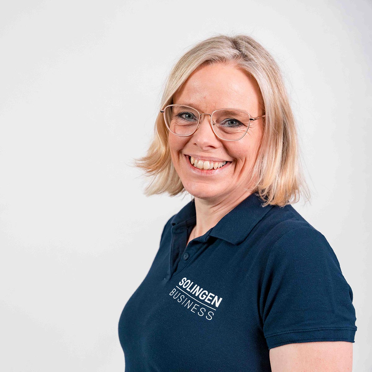 Porträt von Patricia Langhammer, Teammitglied von Solingen.Business, in blauem Poloshirt vor hellem Hintergrund