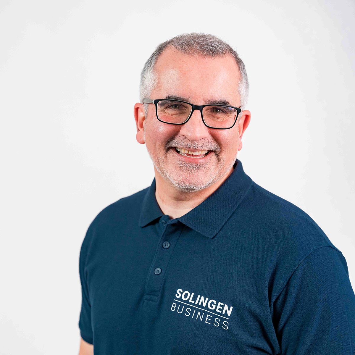 Porträt von Rainer Becker, Teammitglied von Solingen.Business, in blauem Poloshirt vor hellem Hintergrund