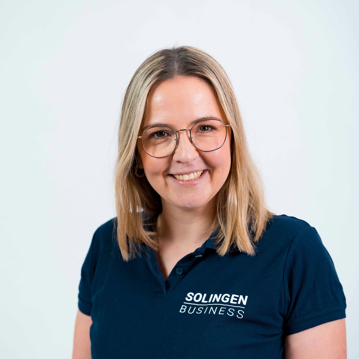 Porträt von Lisa Draeger, Teammitglied von Solingen.Business, in blauem Poloshirt vor hellem Hintergrund