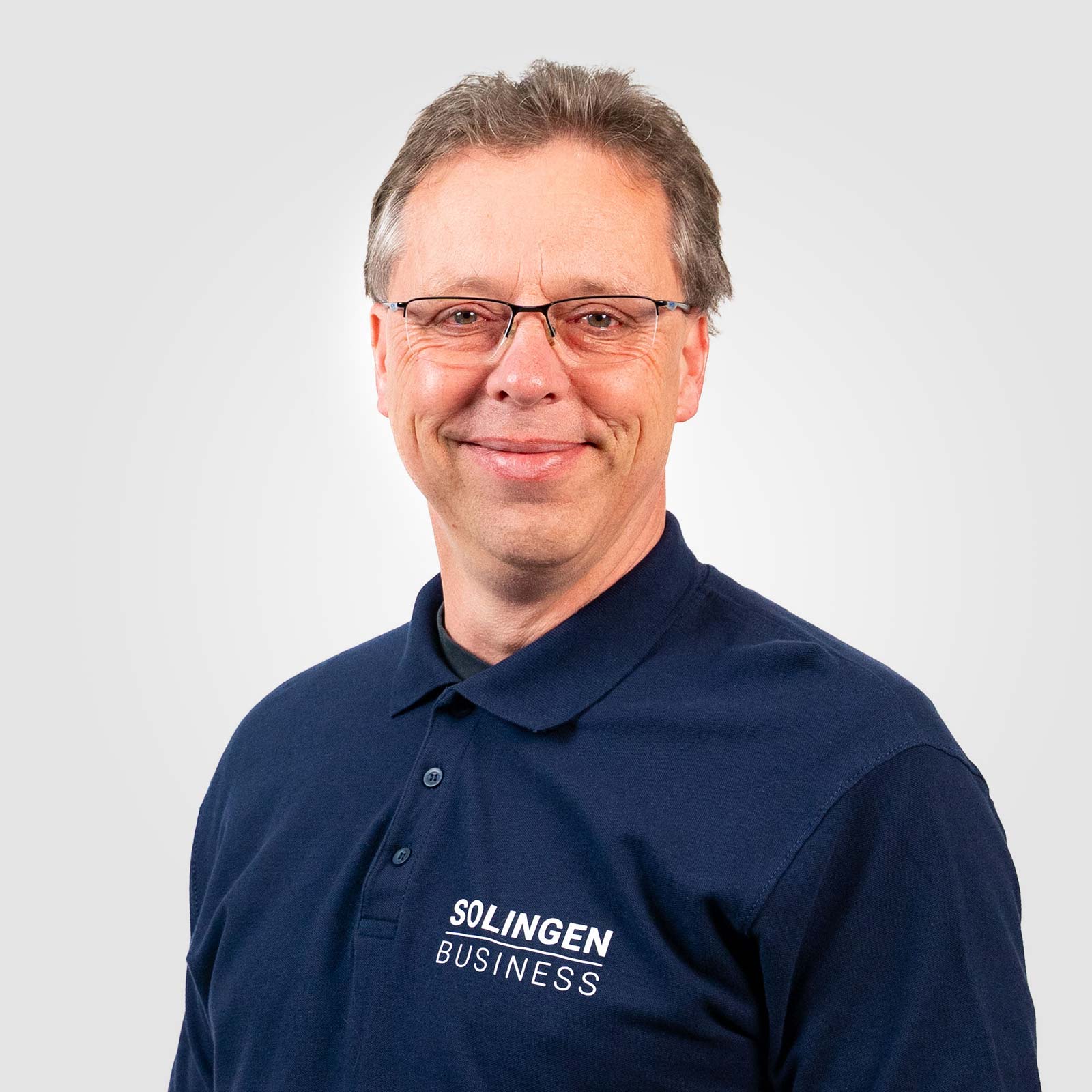 Porträt von Daniel Wieneke, Teammitglied von Solingen.Business, in blauem Poloshirt vor hellem Hintergrund