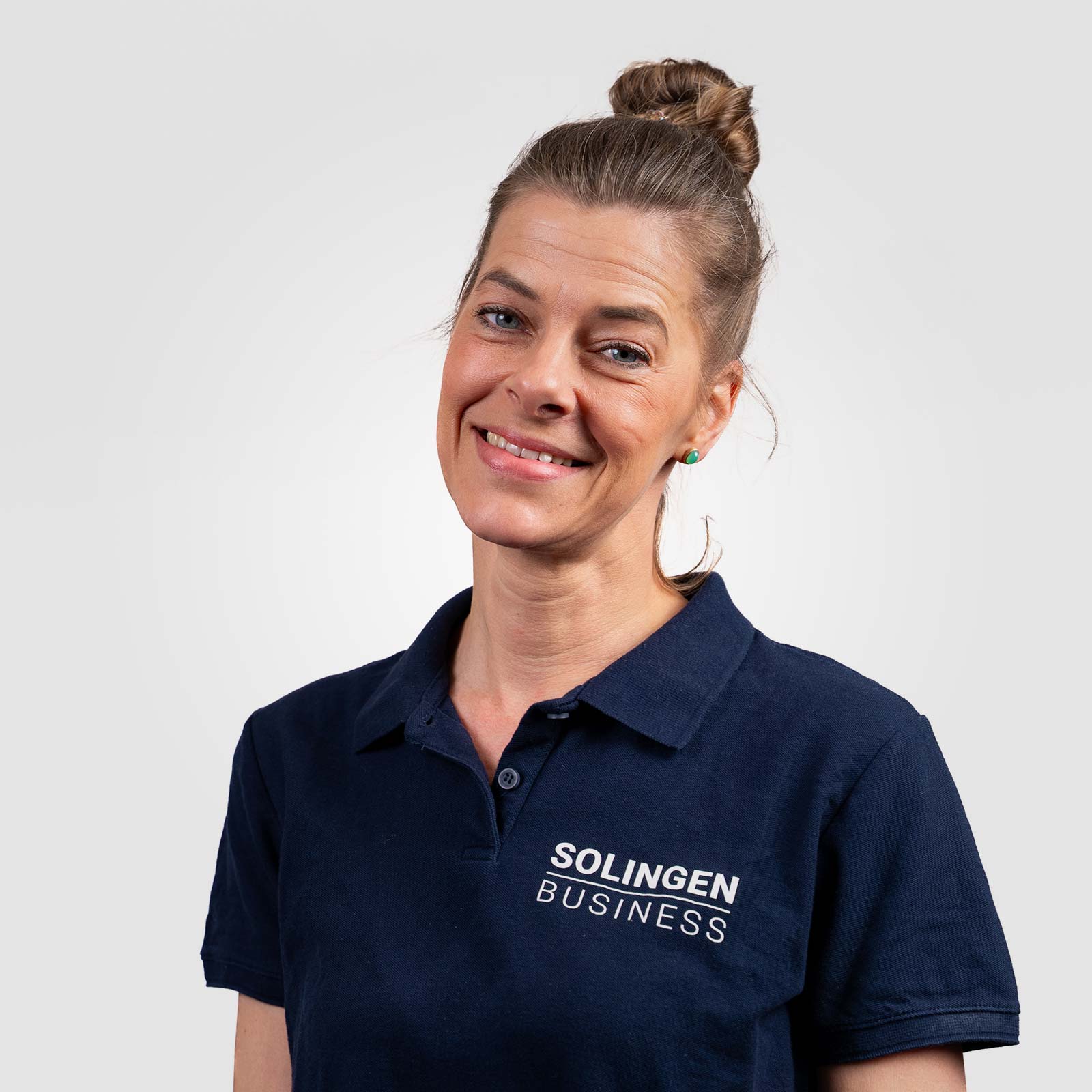 Porträt von Nina Lietzmann, Teammitglied von Solingen.Business, in blauem Poloshirt vor hellem Hintergrund